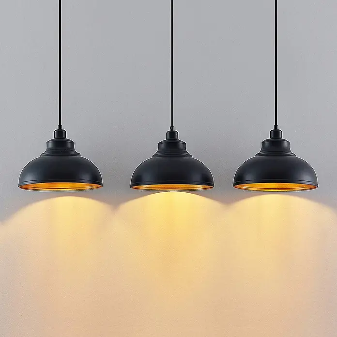 Lindby Pendelleuchte Emna - L x B x H: 101 x 29 x 16 cm, schwarz, Schwarz, gold, E27 - Drei schwarze Pendelleuchten mit goldener Innenseite beleuchten eine Wand mit warmem Licht.