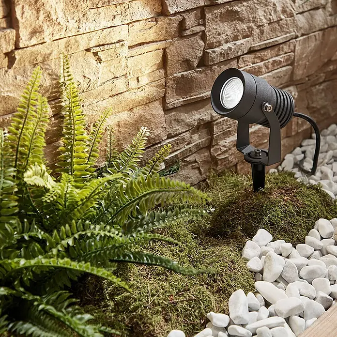 Lucande LED Gartenstrahler mit Erdspieß in dunkelgrau, Strahler Garten -  - Dunkler Metall-Außenstrahler auf einem Erdspieß, beleuchtet eine Steinwand im Gartenbeet.