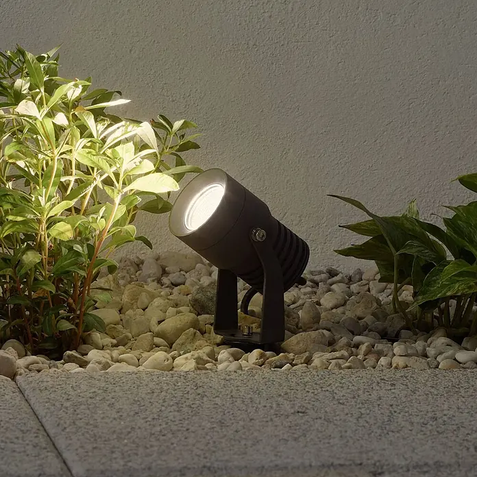 Lucande LED Gartenstrahler mit Erdspieß in dunkelgrau, Strahler Garten -  - Dunkelgrauer Außenstrahler beleuchtet grüne Pflanzen in einem Kiesbeet.