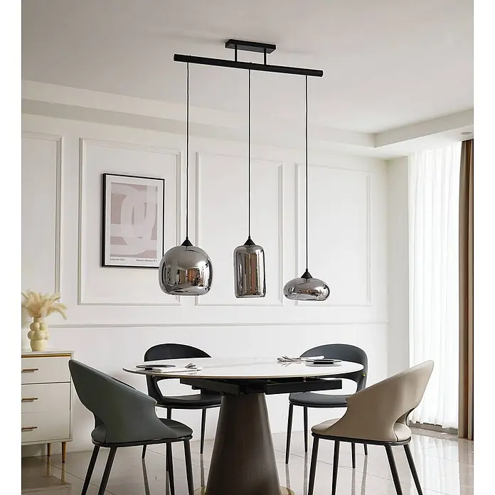 Lindby Pendelleuchte Arloris - alu / grau / zink, rauchgrau, Schwarz, E27 - Drei moderne Pendelleuchten mit reflektierenden rauchgrauen Glasschirmen, die an einer schwarzen Stange über einem weißen Esstisch hängen.