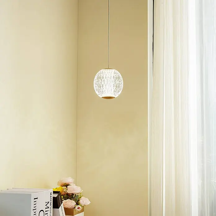 Lucande Pendelleuchte Ismenia - klar / transparent, messing antik, transparent - Beleuchtete kugelförmige Pendelleuchte mit klarem, aufwendig gemustertem Globus und goldenem Sockel, in einem warm getönten Raum hängend.