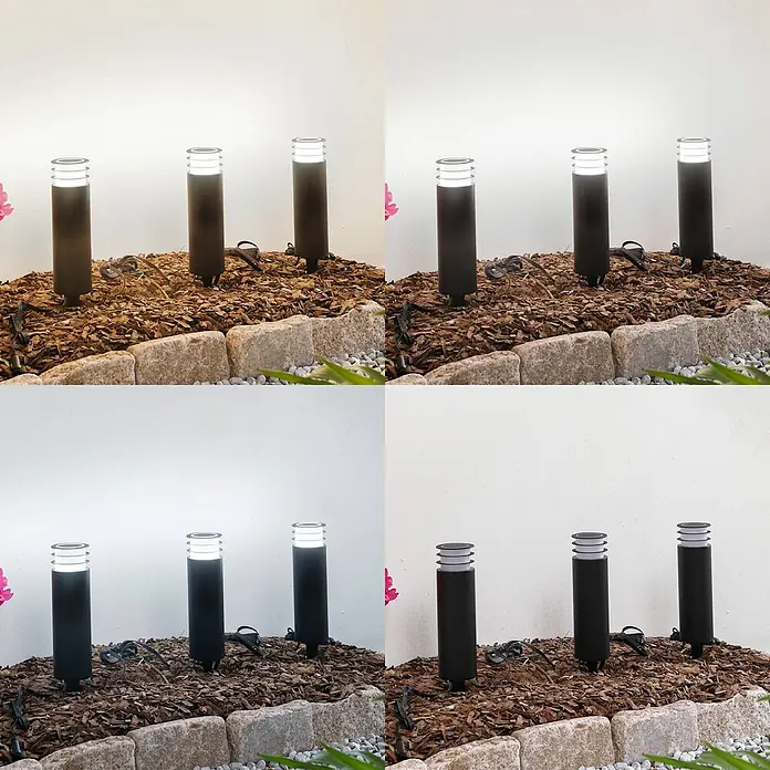Lindby Außensockelleuchte Kaelo -  - Drei schwarze zylindrische Wegeleuchten mit geschichteten Aufsätzen, in einem Gartenbeet mit Rindenmulch.