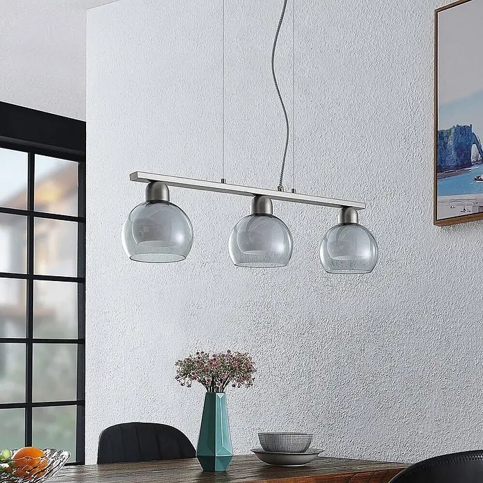 Lucande Pendelleuchte Kaiya - L x B x H: 68 x 14 x 7,8 cm, nickel, weiß, rauchgrau, E14 - Dreiflammige Pendelleuchte mit rauchgrauen Glasschirmen und gebürsteter Metallstange über einem Esstisch.