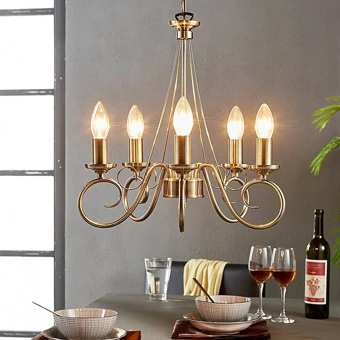 Lindby Kronleuchter Marnia - bronze / altmessing, altmessing, E14 - Antik-messingfarbener Kronleuchter mit 5 kerzenförmigen Lichtern und verschnörkeltem Design über einem Esstisch.