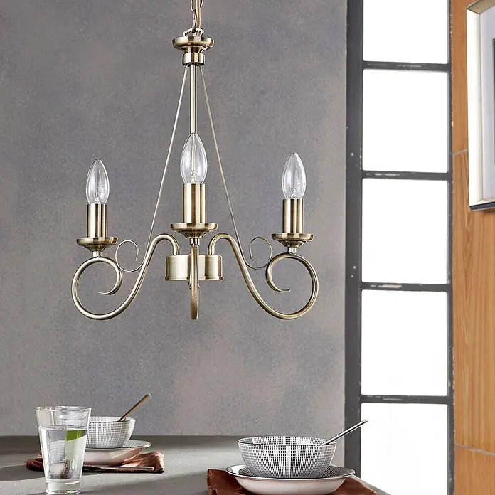 Lindby Kronleuchter Marnia - bronze / altmessing, altmessing, E14 - Messingfarbener Kronleuchter mit drei Kerzenlampen über einem Esstisch hängend.