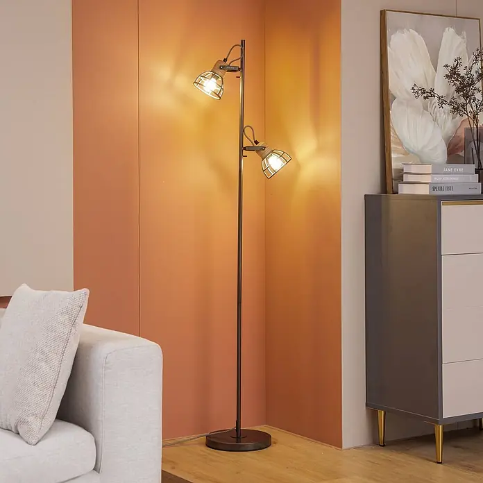 Lindby Stehleuchte Arinthea - Höhe: 153 cm, schwarz, schwarz, E14 - Stehleuchte mit zwei verstellbaren Käfigstrahlern aus dunklem Metall und Holz, die ein modernes Wohnzimmer beleuchtet.