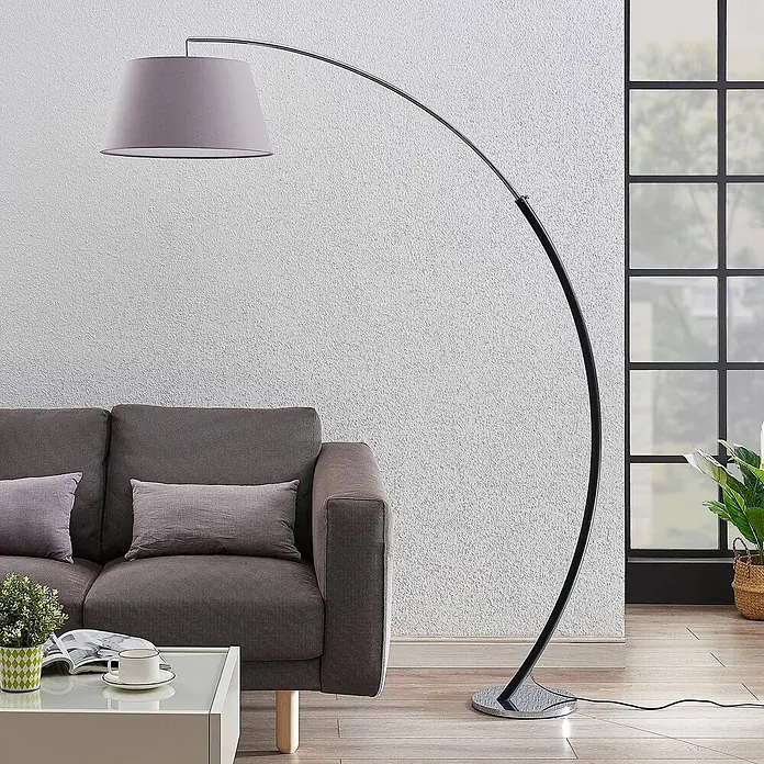 Lucande Stehleuchte Evelyna - Höhe: 192 cm, chrom / silber, alu / grau / zink, E27 - Moderne Bogenlampe mit grauem Stoffschirm und verchromtem/schwarzem Rundfuß, neben einem Sofa im Wohnzimmer.