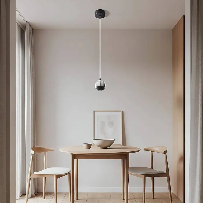 Lucande Pendelleuchte Hayley - klar / transparent, klar, Schwarz - Eine kugelförmige Pendelleuchte mit schwarzem Sockel und strukturierter Glaskugel hängt über einem hellen Holzesstisch.