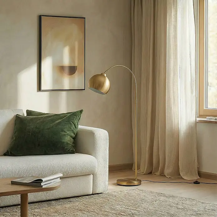 Lindby Stehleuchte Moisia - Höhe: 150 cm, messing / gold, messing / gold, E27 - Elegante goldene Bogenstehleuchte neben einem beigefarbenen Sofa und Fenster in einem modernen Wohnzimmer.