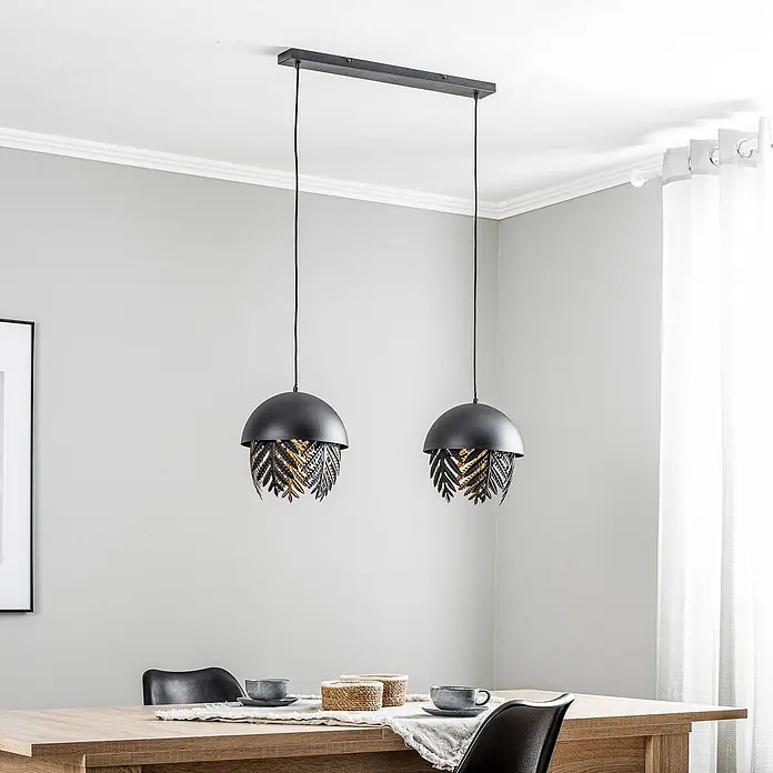 Lucande Pendelleuchte Aparas - L x B x H: 84 x 28 x 35 cm, schwarz, Schwarz, gold, E27 - Zwei schwarze Pendelleuchten mit blattförmigen Dekorationen in Schwarz und Gold über einem Esstisch.