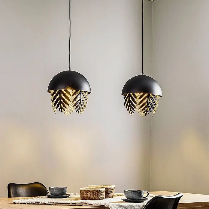 Lucande Pendelleuchte Aparas - L x B x H: 84 x 28 x 35 cm, schwarz, Schwarz, gold, E27 - Zwei schwarze Pendelleuchten mit goldfarbenen Blättern hängen beleuchtet über einem Esstisch.