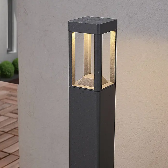 Lucande Außenlaterne Bernd -  - Dunkelgraue, quadratische Pollerleuchte mit strukturierter Oberfläche, spendet warmes Licht auf einer Terrasse.