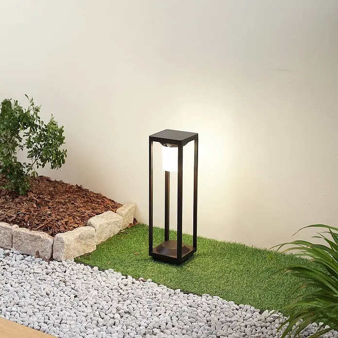 Lucande Außenlaterne Nilea -  - Schwarze Außenstandleuchte mit leuchtend weißem Licht in einer Gartenlandschaft.