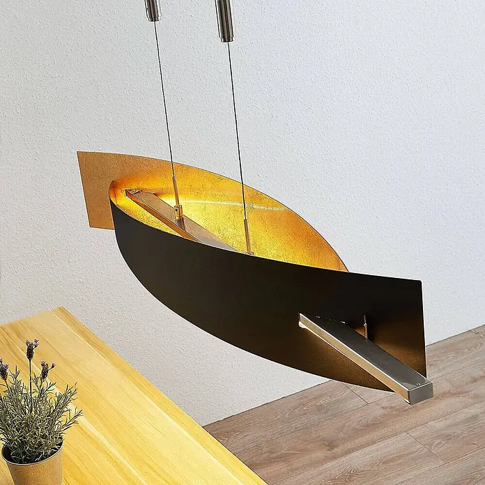 Lucande Pendelleuchte Marija - L x B x H: 101 x 18,5 x 1,8 cm, schwarz, Schwarz, gold - Eine stilvolle gold-schwarze gebogene Pendelleuchte hängt über einem Holztisch und beleuchtet diesen.