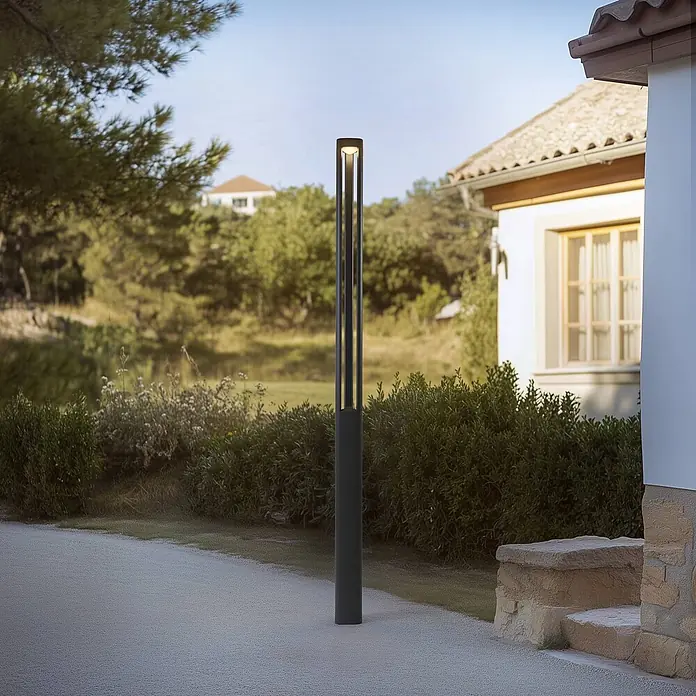 Lucande Außenlaterne Pirron -  - Hohe, dunkelgraue Pollerleuchte aus Metall mit integrierter Beleuchtung, neben einem Gartenweg vor einem Haus.