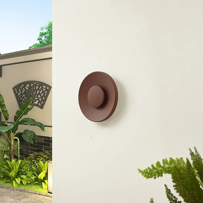 Lucande Außenwandleuchte Kayana - braun / rost, IP65 - Braune runde Außenwandleuchte an einer weißen Wand in einer Gartenumgebung montiert.