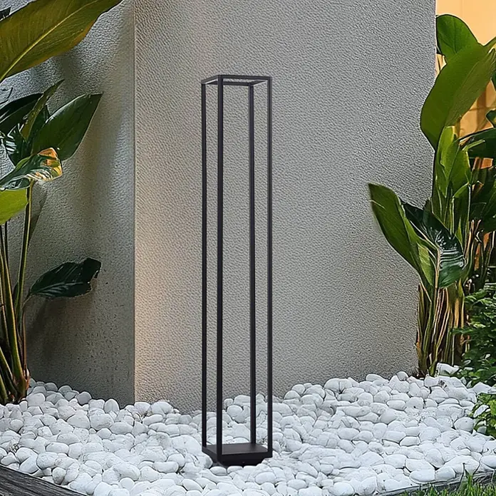 Lucande Außenlaterne Thorvid -  - Hohe, schwarze, rechteckige Außenlampe mit offenem Rahmen, steht auf weißen Kieselsteinen zwischen grünen Pflanzen.