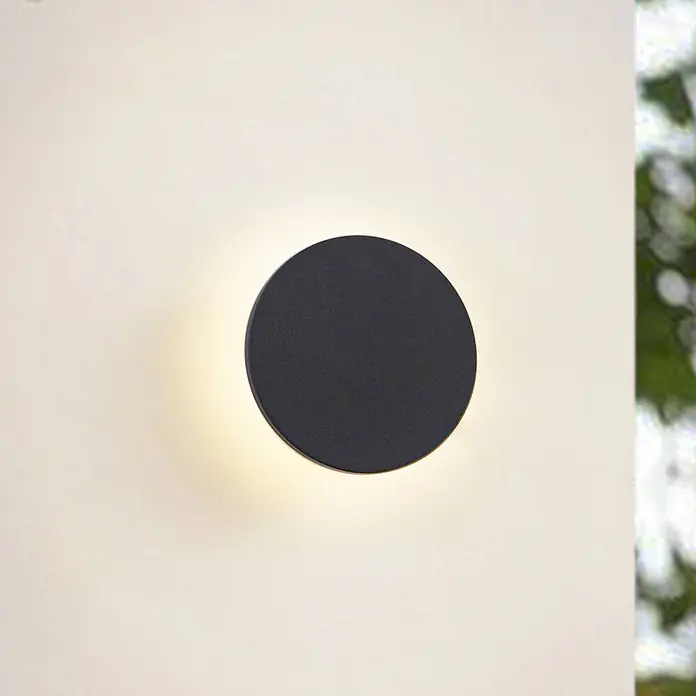 Arcchio Außenwandleuchte Gravo - schwarz, IP65 - Eine schwarze runde Wandleuchte, die einen warmen Lichtkranz abgibt.