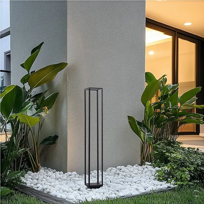 Lucande Außenlaterne Thorvid -  - Schwarze, minimalistische, rechteckige Außenbodenlampe beleuchtet einen modernen Gartenweg mit weißen Kieselsteinen und Grünpflanzen.