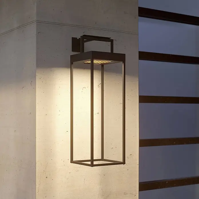 Lucande Außenlaterne Lynzy -  - Moderne rechteckige dunkle Metall-Außenwandleuchte an einer Betonwand, die warmes Licht nach unten wirft.
