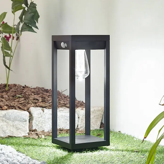 Lindby Außenlaterne Enea -  - Schwarze, rechteckige Außenlampe mit sichtbarer Glühbirne und Sensoren im Garten.