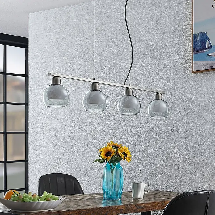 Lucande Pendelleuchte Kaiya - L x B x H: 95 x 14 x 7,8 cm, nickel, weiß, rauchgrau, E14 - Vierflammige Pendelleuchte mit gebürsteter Metallschiene und grau getönten Glaskugeln, über einem Esstisch.