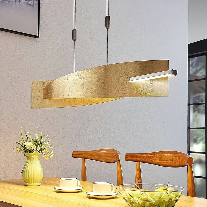 Lucande Pendelleuchte Marija - L x B x H: 101 x 18,5 x 1,8 cm, messing / gold, gold, silber - Elegante Hängeleuchte in Blattgold-Optik mit integrierter LED-Leiste, die über einem Holzesstisch hängt und den Bereich beleuchtet.