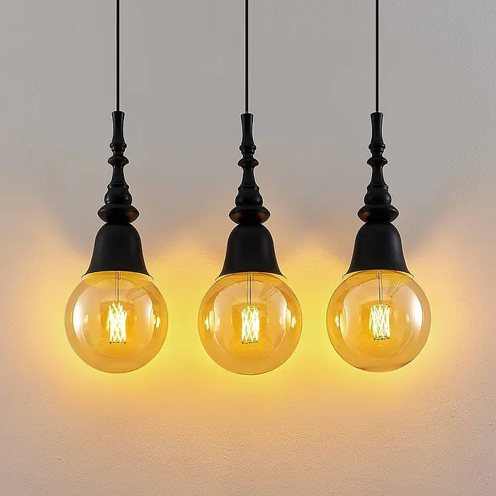 Lucande Pendelleuchte Gesja - L x B x H: 63,5 x 13,5 x 32,5 cm, Schwarz, E27 - Drei Hängelampen aus schwarzem Metall und bernsteinfarbenem Glas hängen von der Decke und leuchten warm.