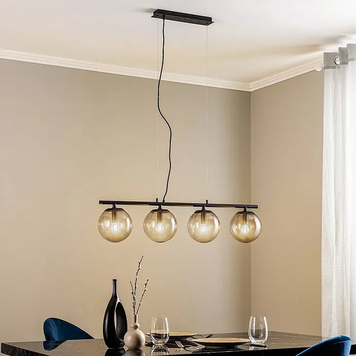 Lucande Pendelleuchte Sotiana - L x B x H: 96 x 18 x 18 cm, alu / grau / zink, rauchgrau, Schwarz, E14 - Schwarze Pendelleuchte aus Metall mit vier bernsteinfarbenen Glaskugeln über einem Esstisch.