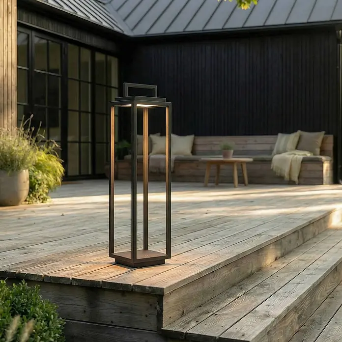Lucande Außenstehleuchte Elaja -  - Hohe, dunkle Metall-Gartenlaterne spendet warmes Licht auf einer Holzterrasse neben Stufen.