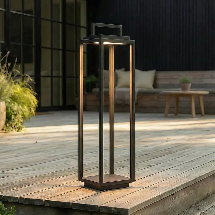 Lucande Außenstehleuchte Elaja -  - Dunkle rechteckige Outdoor-Laterne aus Metall auf Holzterrasse, strahlt warmes Licht aus.