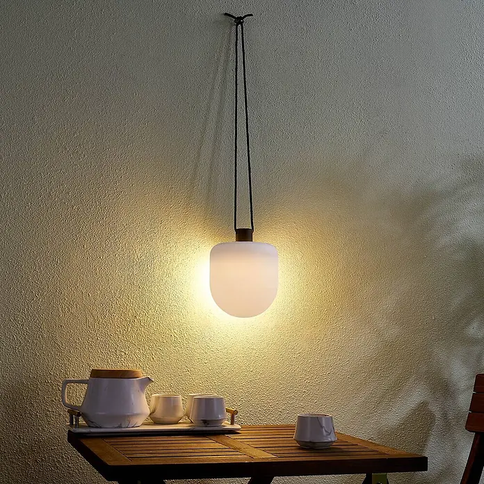 Lindby Außenwand- & Deckenleuchte Eleia - weiß / opal, IP44 - Mattweiße Pendelleuchte beleuchtet einen Tisch mit Teekanne und Tassen.