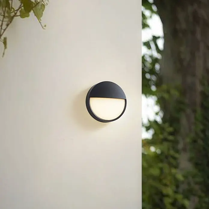 Arcchio Außenwandleuchte Gravo - schwarz, IP65 - Eine runde schwarze Außenwandleuchte mit nach unten gerichtetem Lichtschein an einer hellen Wand montiert.