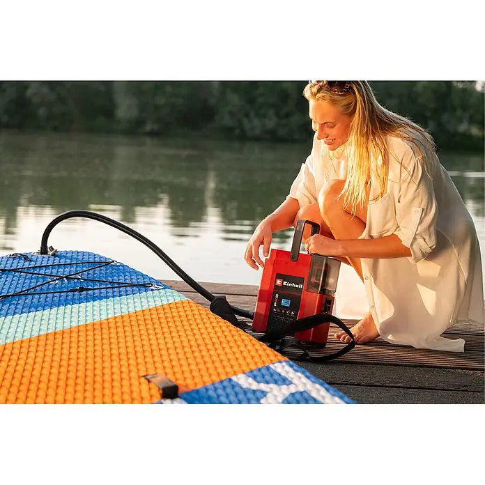Einhell Akku-Kompressor Suppero 18/380 - 18 V, 1,38 bar - Rote und schwarze Einhell-Pumpe bläst ein Paddleboard auf, bedient von einer Frau am See.