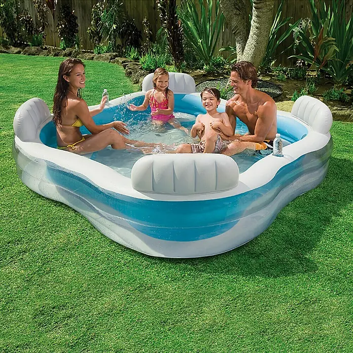 Intex Piscina Quick-Up Family Lounge - L x An x Al: 229 x 229 x 66 cm, Azul/Blanco, 880 l - Esta toma muestra una piscina inflable con una familia en un jardín. La piscina es azul y blanca y tiene asientos con respaldos.
