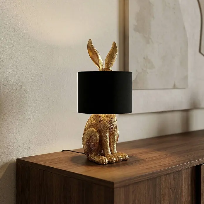 Lindby Tischleuchte Lorentina - L x B x H: 24 x 24 x 57 cm, messing / gold, schwarz, E27 - Goldene Hasen-Tischlampe mit schwarzem Schirm auf einem Holzschrank.