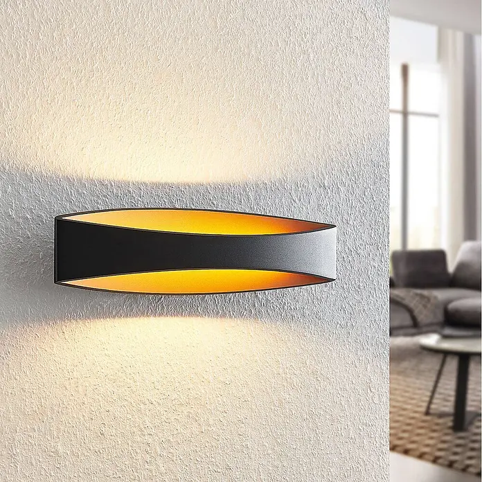 Arcchio Wandleuchte Jelle - schwarz, schwarz - Schwarze Wandleuchte mit goldener Innenseite, die warmes Licht nach oben und unten auf eine strukturierte Wand wirft.