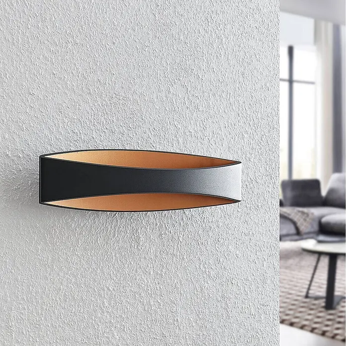 Arcchio Wandleuchte Jelle - schwarz, schwarz - Schwarze geschwungene Wandleuchte mit Kupfer-Innenseite, an texturierter Wand montiert.