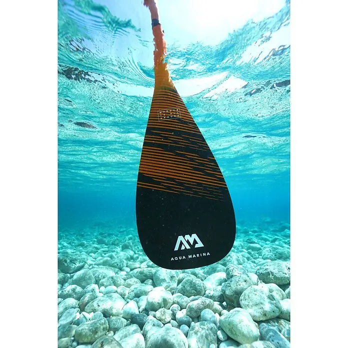Aqua Marina SUP-Paddel Carbon X - 1 Stk., Verstellbar: 180 cm - 200 cm - Aqua Marina Paddelblatt, schwarz mit orangefarbenen Streifen, teilweise in klarem blauen Wasser über einem Felsgrund.