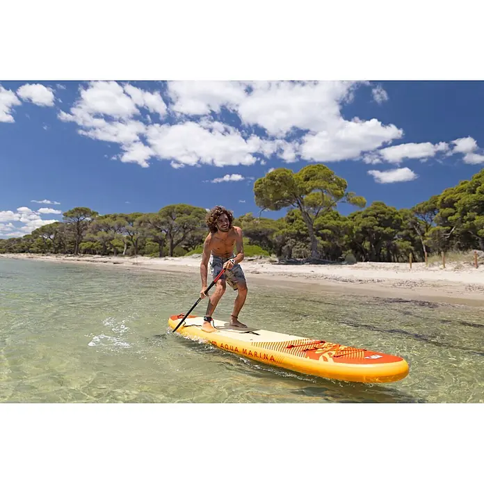 Aqua Marina SUP-Board-Set Fusion - L x B x H: 330 x 81 x 15 cm, Orange, Tragkraft: 150 kg - Ein Mann paddelt auf einem gelb-orangen Aqua Marina Stand-Up-Paddleboard in klarem Wasser an einem Sandstrand.