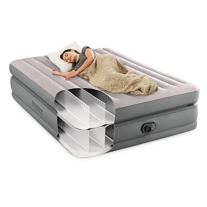 Intex Luftbett Queen Comfort - L x B x H: 203 x 152 x 51 cm, Grau, Integrierte Luftpumpe - Graues Intex Luftbett mit Schnittansicht der Fiber-Tech-Konstruktion, darauf schläft eine Frau gemütlich unter einer beigen Decke.
