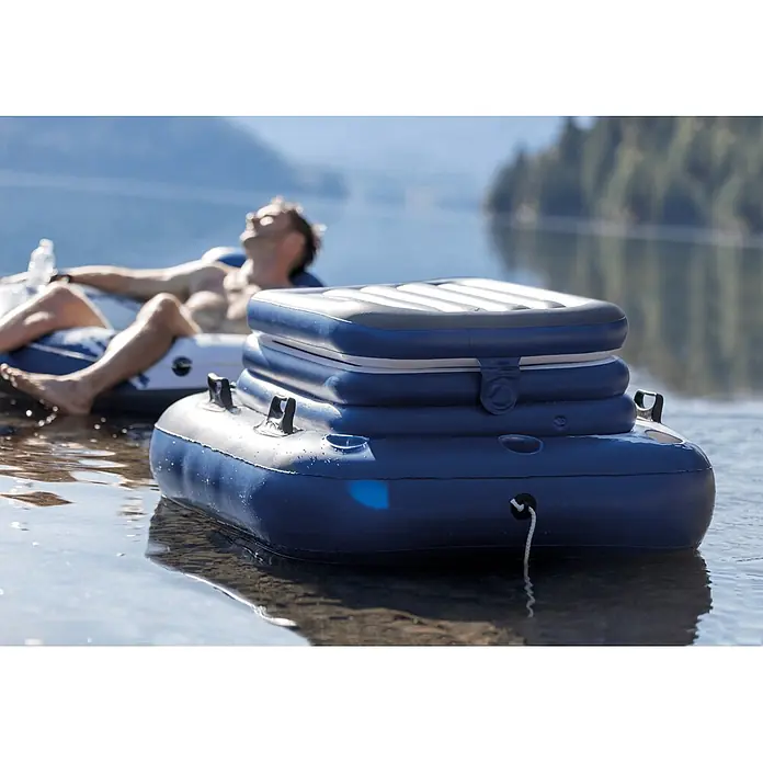 Intex Kühlbox Mega Chill 2 - Grau, Weiß, Blau, L x B x H: 114 x 86 x 42 cm - Blau-weiße aufblasbare Kühlbox schwimmt auf Wasser, mit Seil befestigt, daneben eine Person auf einem Schwimmkörper entspannend.