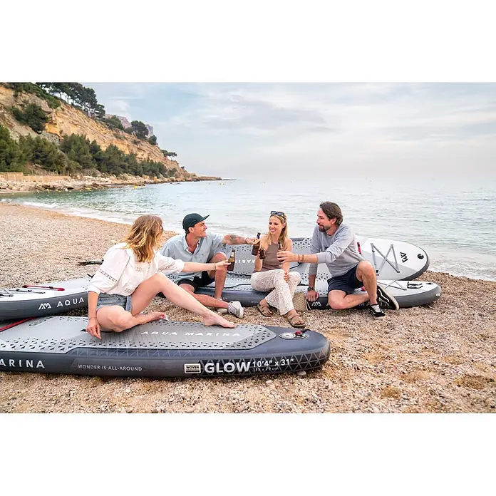 Aqua Marina SUP-Board-Set Glow - L x B x H: 315 x 79 x 15 cm, Grau, Tragkraft: 140 kg - Vier Personen entspannen auf grauen und weißen Aqua Marina aufblasbaren Paddleboards am Kiesstrand.