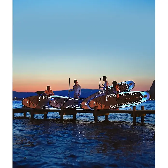 Aqua Marina SUP-Board-Set Glow - L x B x H: 315 x 79 x 15 cm, Grau, Tragkraft: 140 kg - Menschen auf einem Steg bei Sonnenuntergang mit beleuchteten Paddleboards, bereit zum Nachtpaddeln.