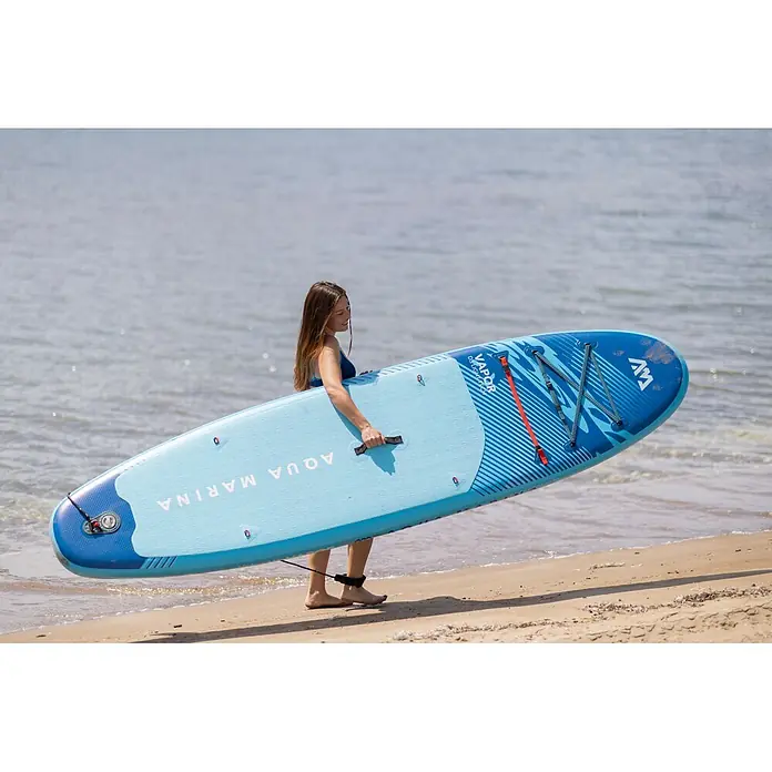 Aqua Marina SUP-Board-Set Vapor - L x B x H: 315 x 79 x 15 cm, Blau, Tragkraft: 140 kg - Eine Frau trägt ein hell- und dunkelblaues Aqua Marina Vapor Paddleboard mit strukturierter Deckauflage am Sandstrand.