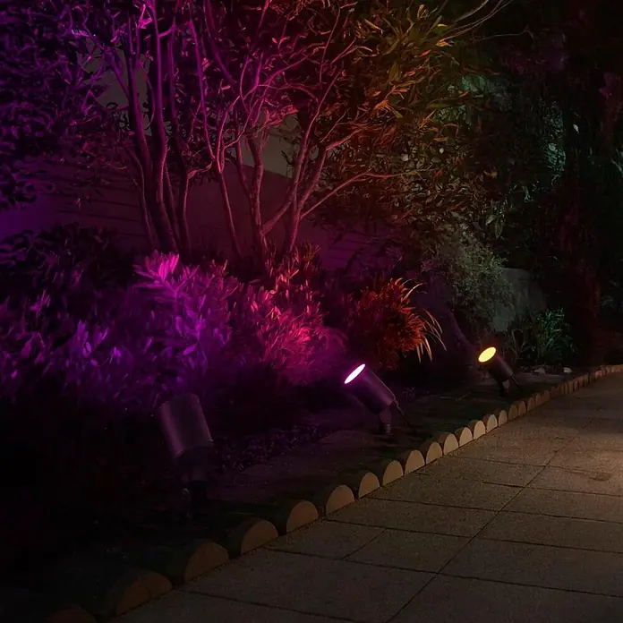 Hama LED-Gartenstrahler WLAN Gartenstecker - Schwarz - Dunkle Outdoor-Strahler beleuchten Pflanzen in leuchtenden Farben entlang eines Gartenweges bei Nacht.