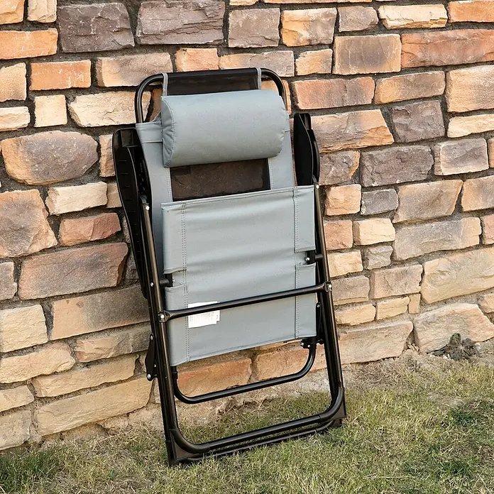 Outsunny Gartenstuhl-Set - 2 Stk., Oxfordstoff, Klappbar, Grau, B x T x H: 70 x 70 x 109 cm - Geklappter grauer Liegestuhl mit schwarzem Gestell und Kopfstütze, lehnt an einer Steinmauer auf Gras.