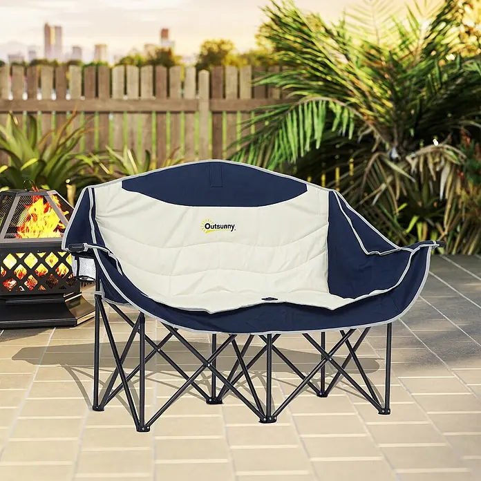 Outsunny Campingstuhl - Metall, Oxfordstoff, Klappbar, Blau - Marineblau-cremefarbener gepolsterter Klapp-Outdoor-Liegesessel mit Getränkehalter, auf einer Terrasse neben einer Feuerstelle.