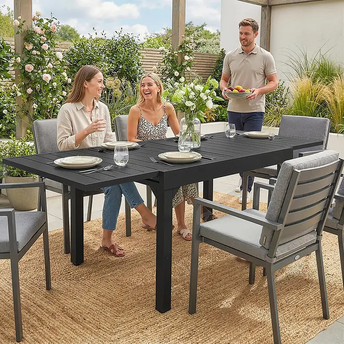 Outsunny Gartentisch - L x B x H: 160 x 80 x 75 cm, Aluminium, Stahl, Schwarz - Dunkelgraues Outdoor-Essset aus Metall mit passenden Stühlen und grauen Kissen, im Garten in Gebrauch gezeigt.