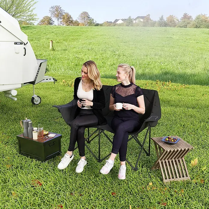Outsunny Campingstuhl - 600D Oxford-Gewebe, Metall, Klappbar, Schwarz - Zwei Frauen entspannen auf einem schwarzen Klappstuhl für zwei Personen im Freien.